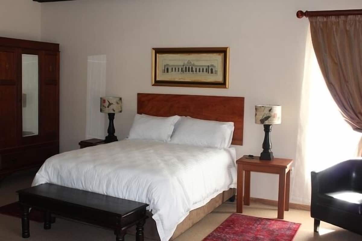 Une chambre à coucher avec un grand lit, deux tables de chevet avec des lampes, une tête de lit en bois, un tableau encadré au mur, un banc et une chaise.