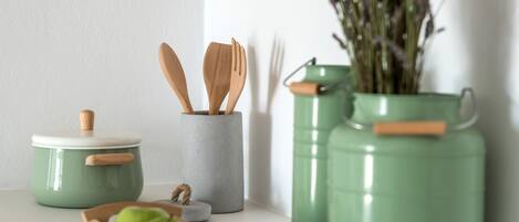 A kitchen area with a green pot, wooden utensils, a bowl of green apples, and a vase with lavender.