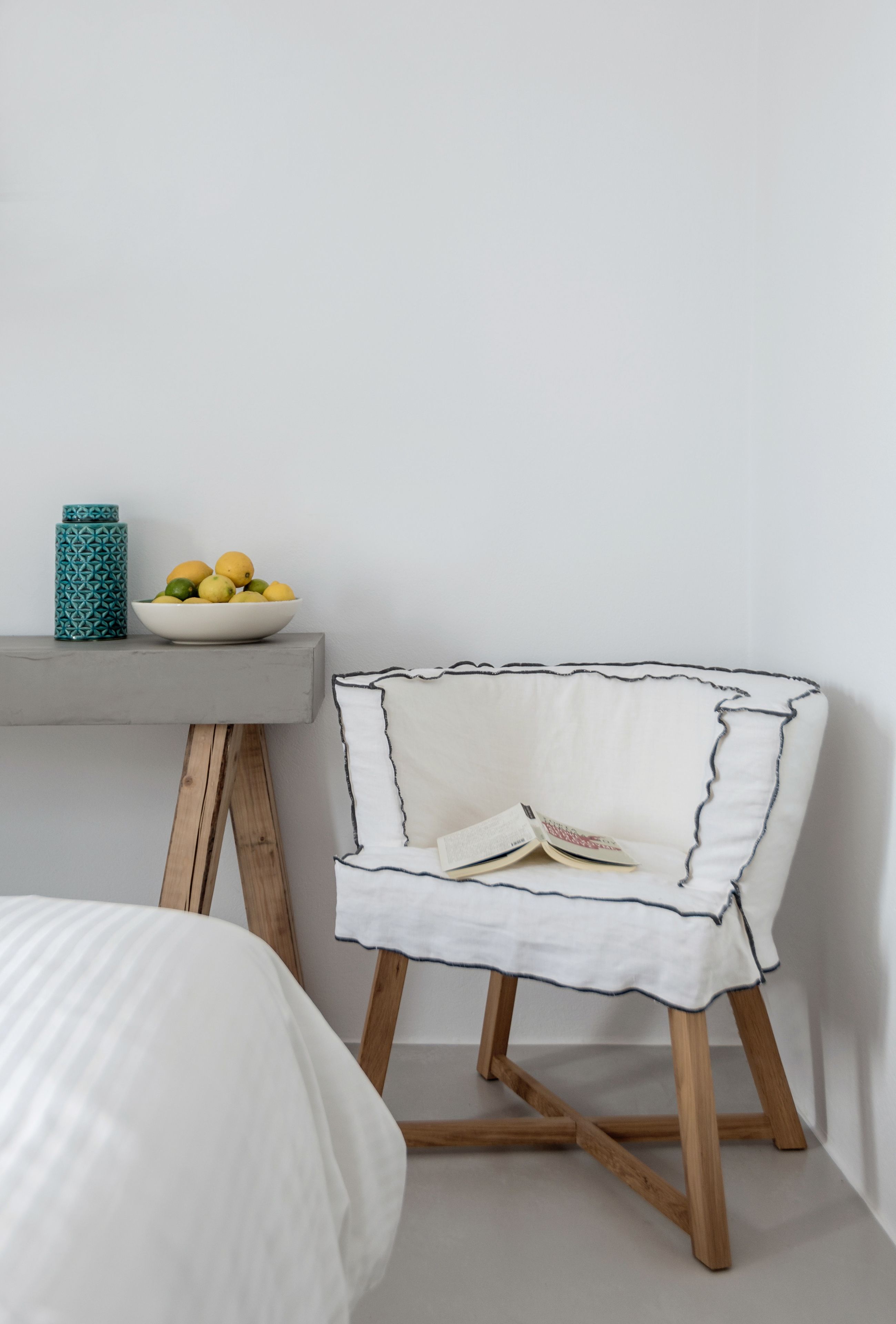 Un rincón de una habitación con una silla blanca, una mesita con un frutero, y un jarrón estampado.