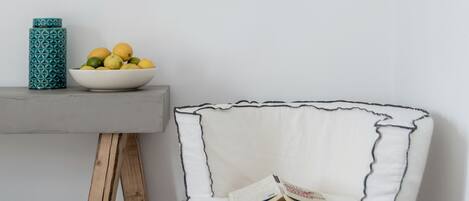 Un rincón de una habitación con una silla blanca, una mesita con un frutero, y un jarrón estampado.
