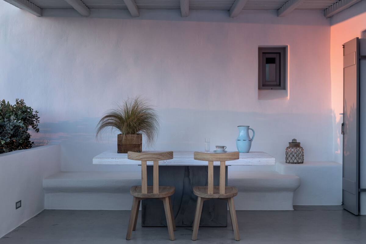 A modern outdoor seating area with two wooden stools, a white table, and a potted plant.