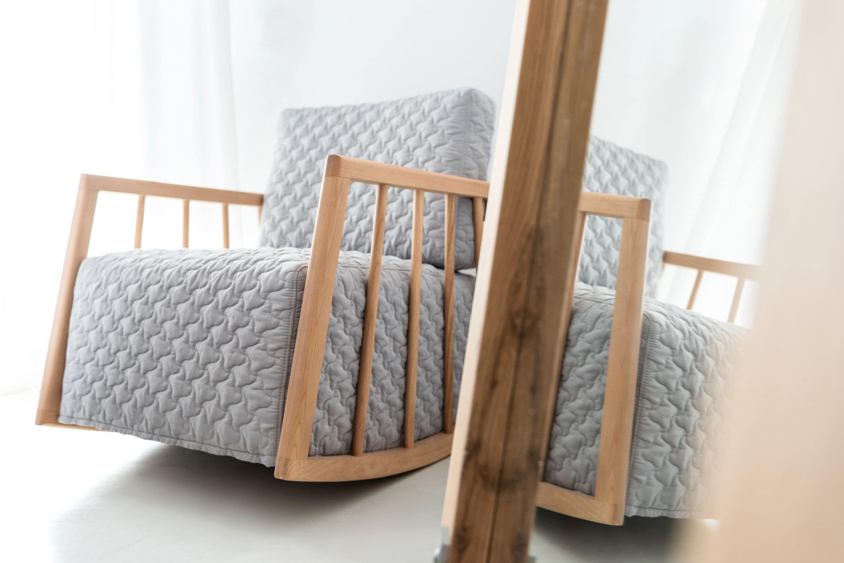 A wooden-framed chair with a quilted grey cushion.