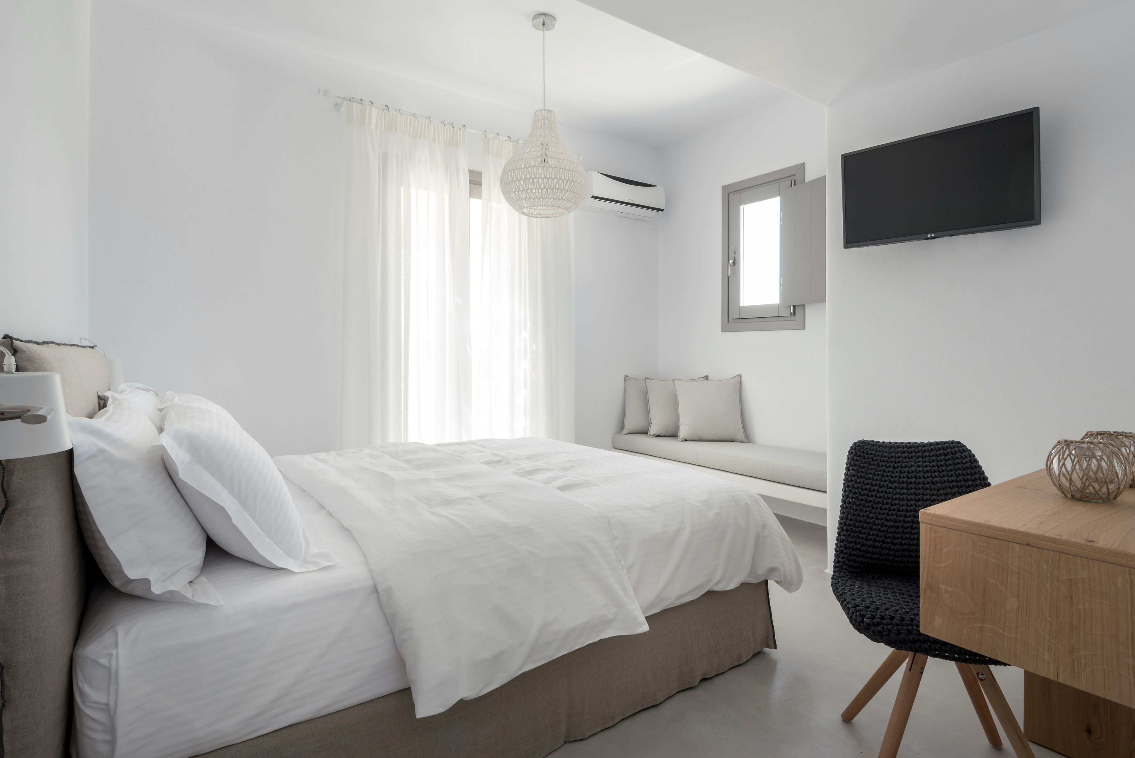 A modern bedroom with a bed, bedside table, chair, and a TV on the wall.