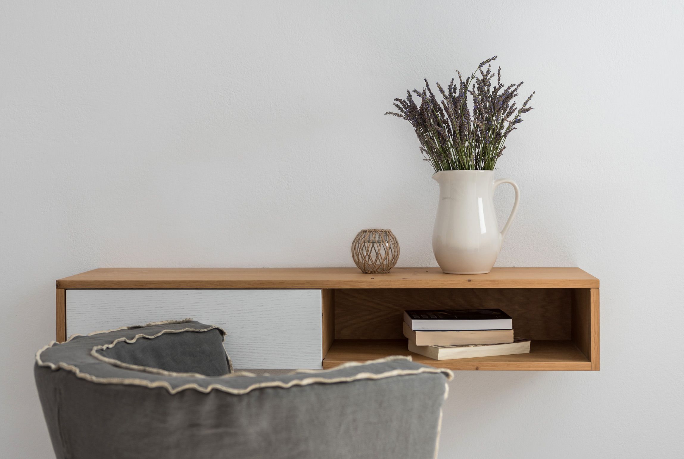 A minimalist room with a wooden shelf holding books and a vase with dried flowers.