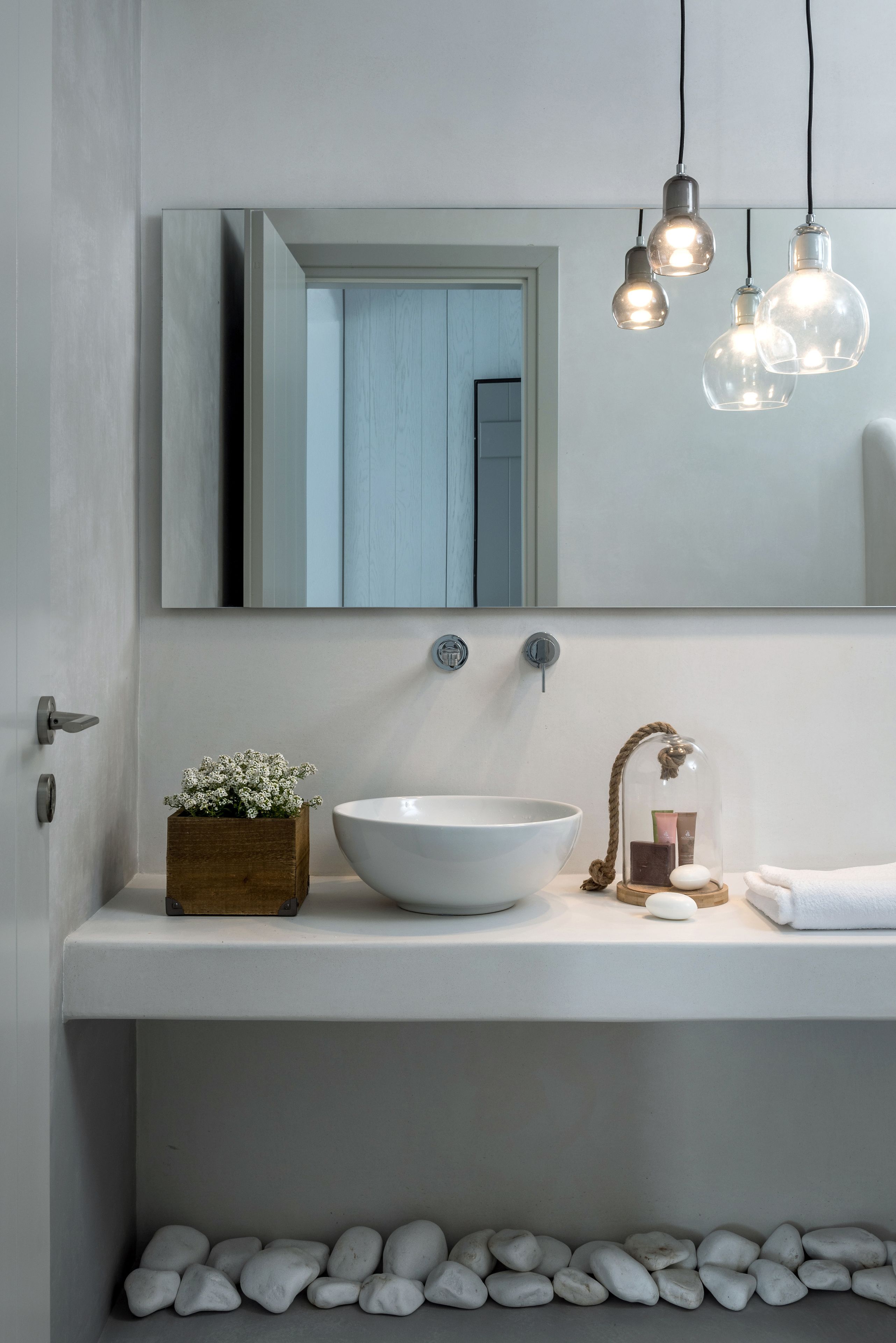 A modern bathroom with a white sink, a mirror, and a wooden planter with flowers.