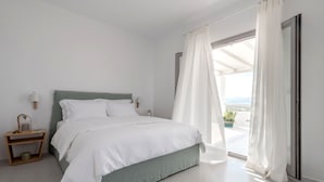 Un dormitorio moderno con cama, mesita de noche, ventana con cortinas traslúcidas y vistas al exterior.