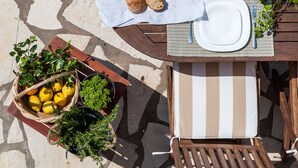 A stone-tiled patio with a wooden table set for a meal, including plates, cutlery, and a basket of lemons and herbs. - Penelope Villas (Kefalonia)