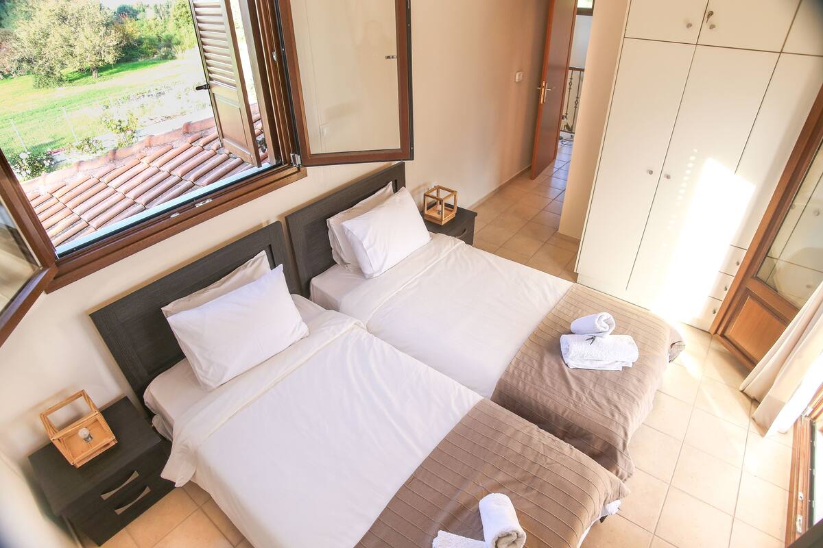A bedroom with two beds, a window with a view of a garden, and a wardrobe.