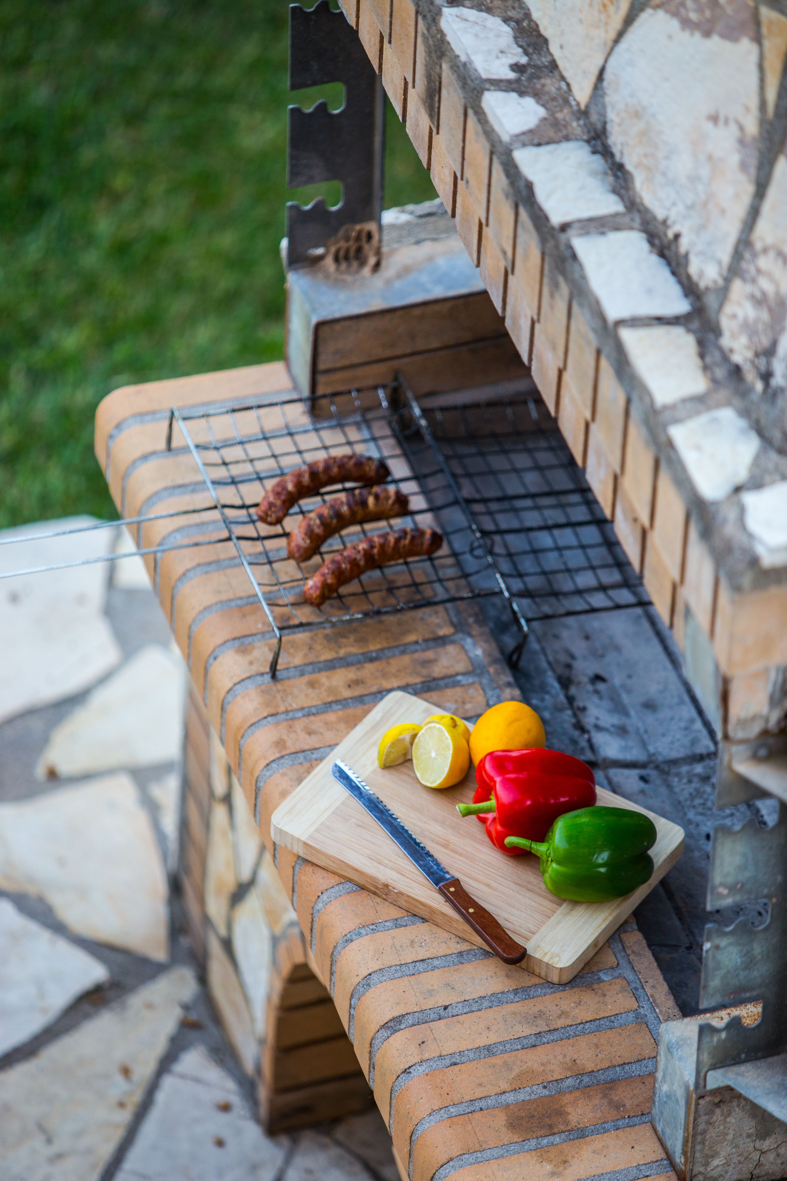 A brick barbecue grill with sausages and vegetables.
