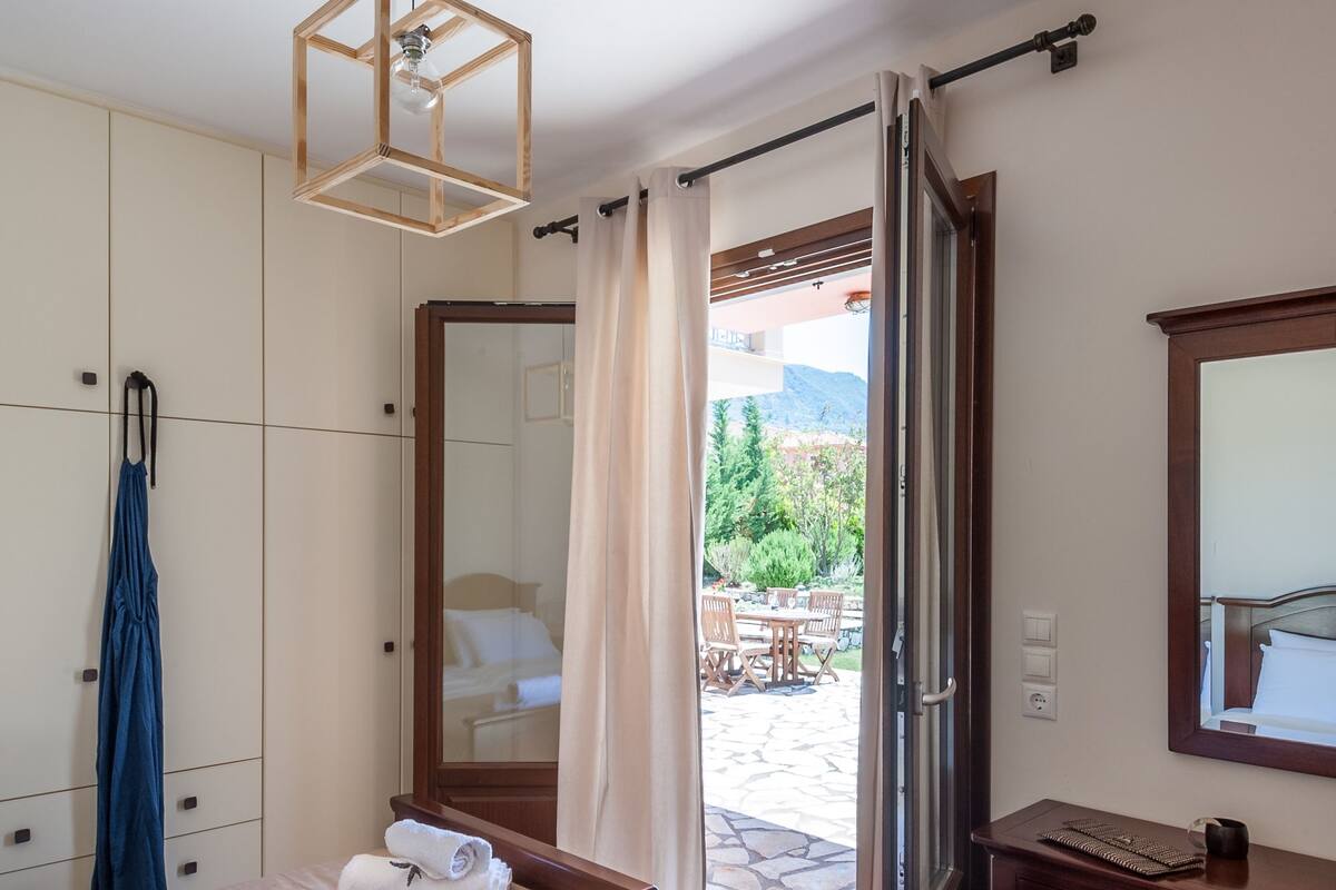 A hotel room with two beds, a wooden ceiling light, a mirror, a bathroom with a sink, and a view of an outdoor patio.