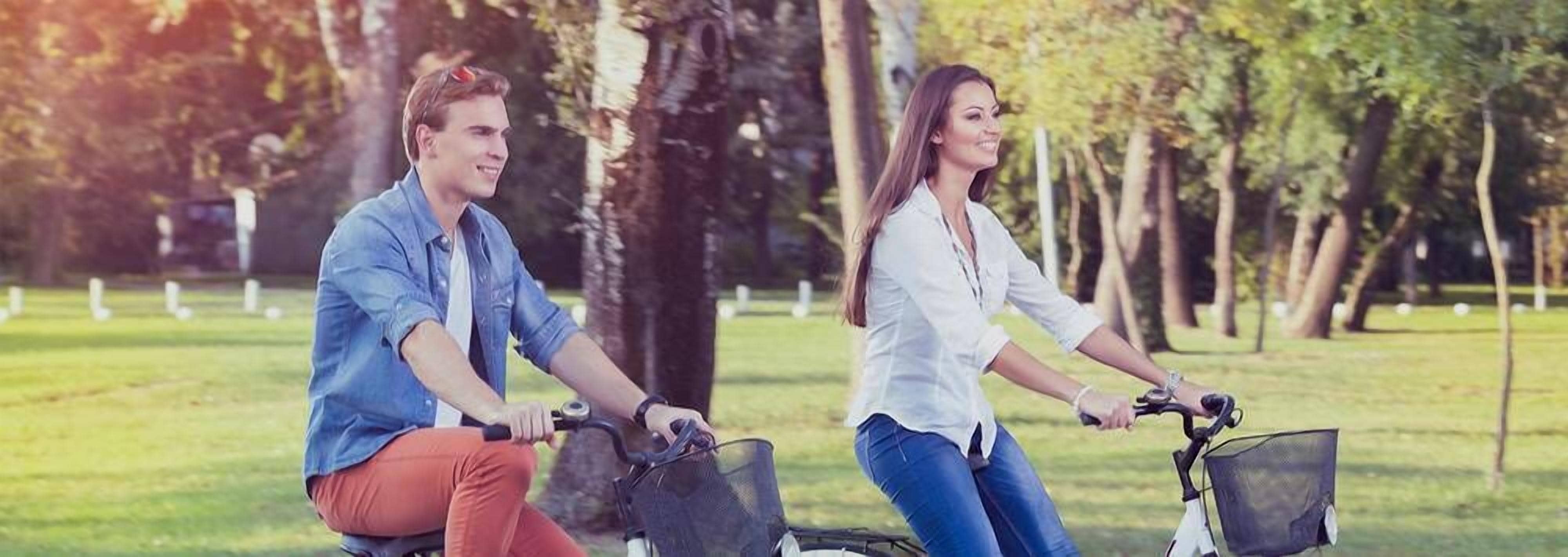 Duas pessoas andando de bicicleta em um parque com árvores e grama.