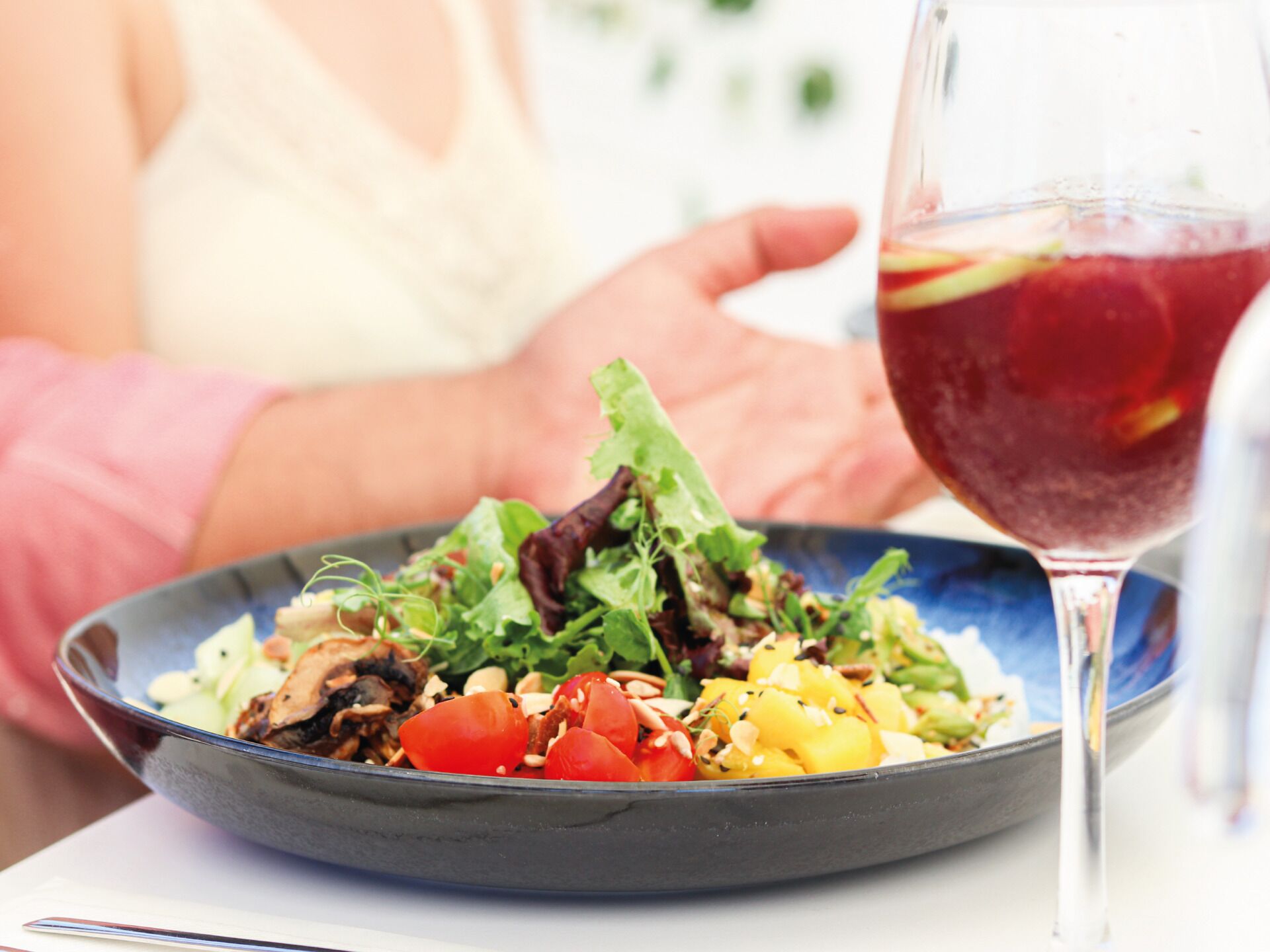 A bowl of salad with a glass of red drink beside it.