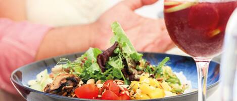 Insalata in una ciotola con un bicchiere di bevanda rossa accanto.