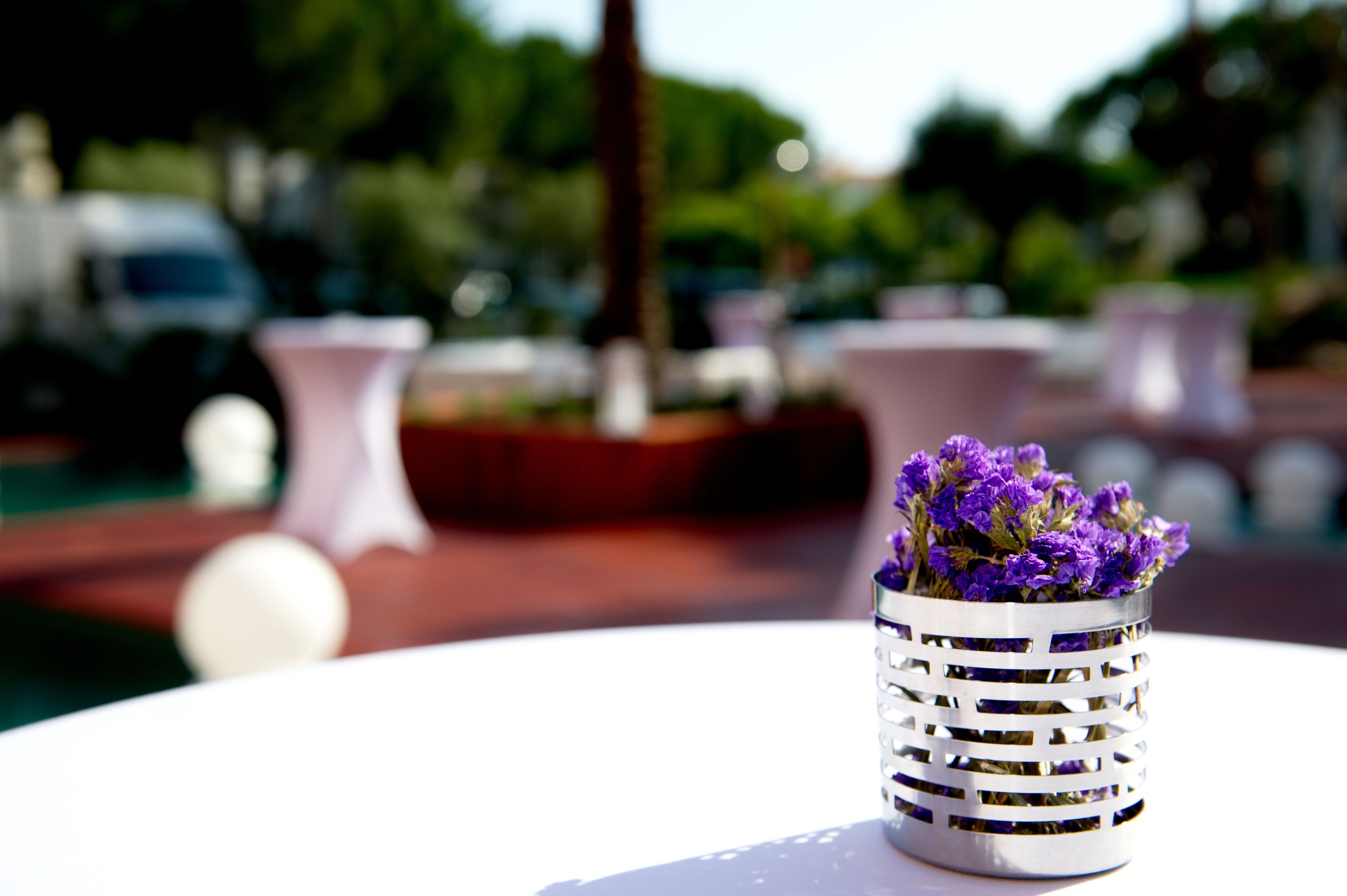 Una mesa blanca con un florero metálico que contiene flores púrpuras.