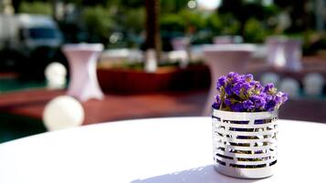 Una mesa blanca con un florero metálico que contiene flores púrpuras.