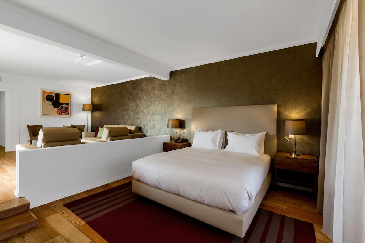 Habitació d'hotel moderna amb un llit gran, un sofà, escriptori i una làmpada.