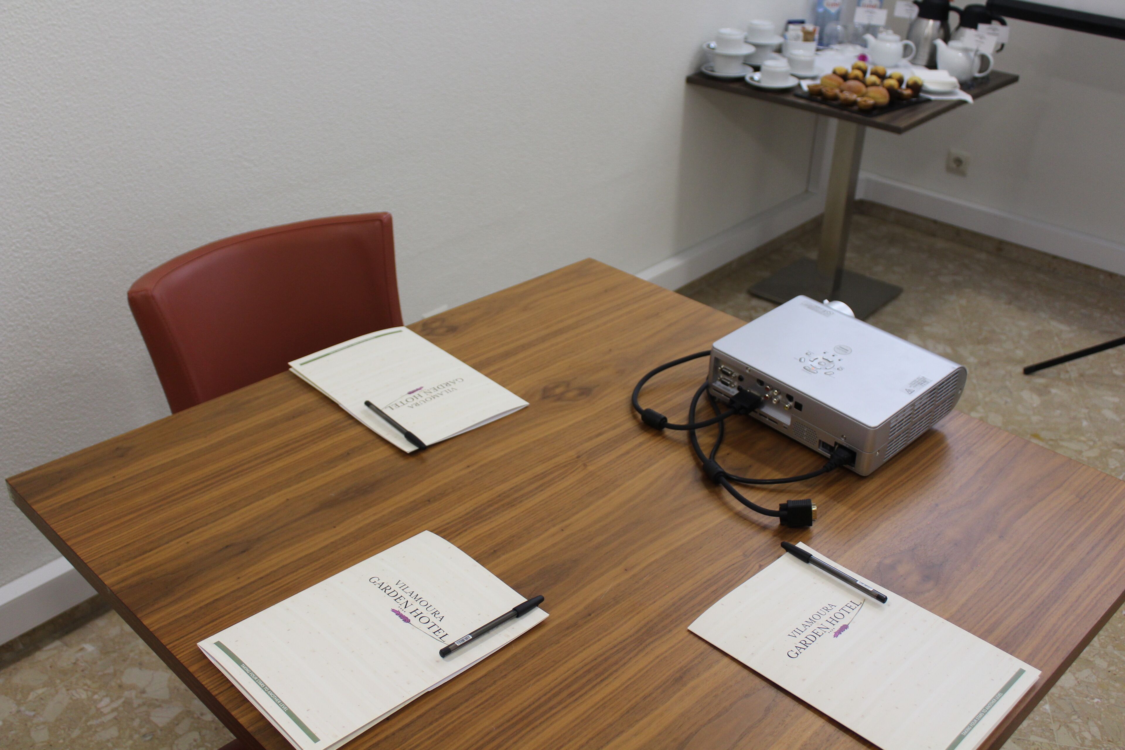 Une table de conférence équipée d’un projecteur, de deux blocs-notes et de stylos.