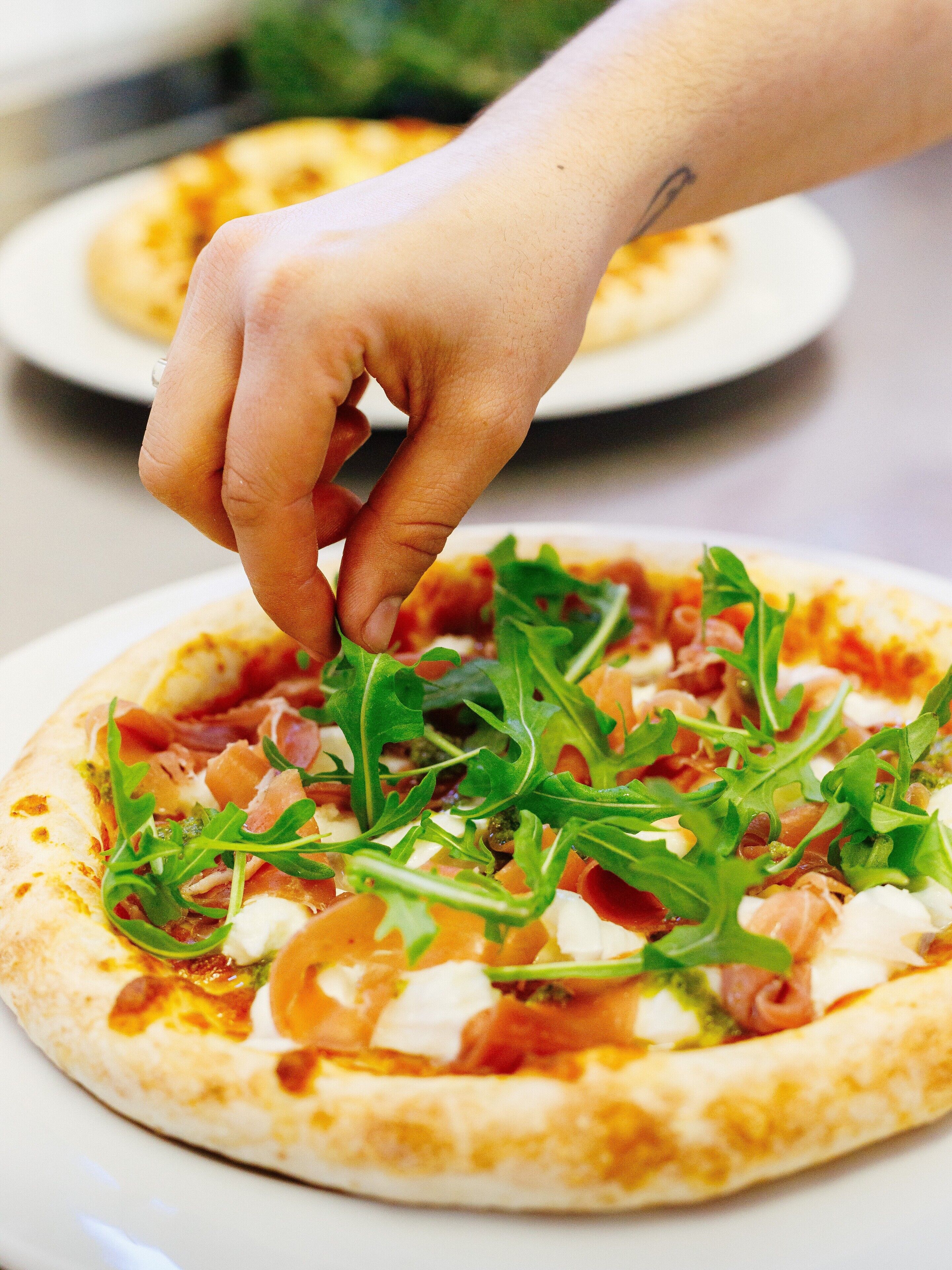 Käsi asettelee rucolaa pizzan päälle.