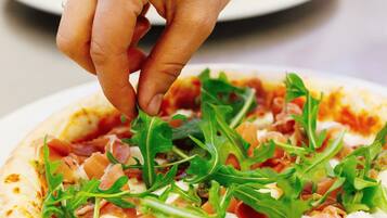 A hand placing arugula on a pizza.