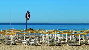 Een strand met rijen gele parasols en witte ligbedden, een rederspost en de oceaan op de achtergrond.