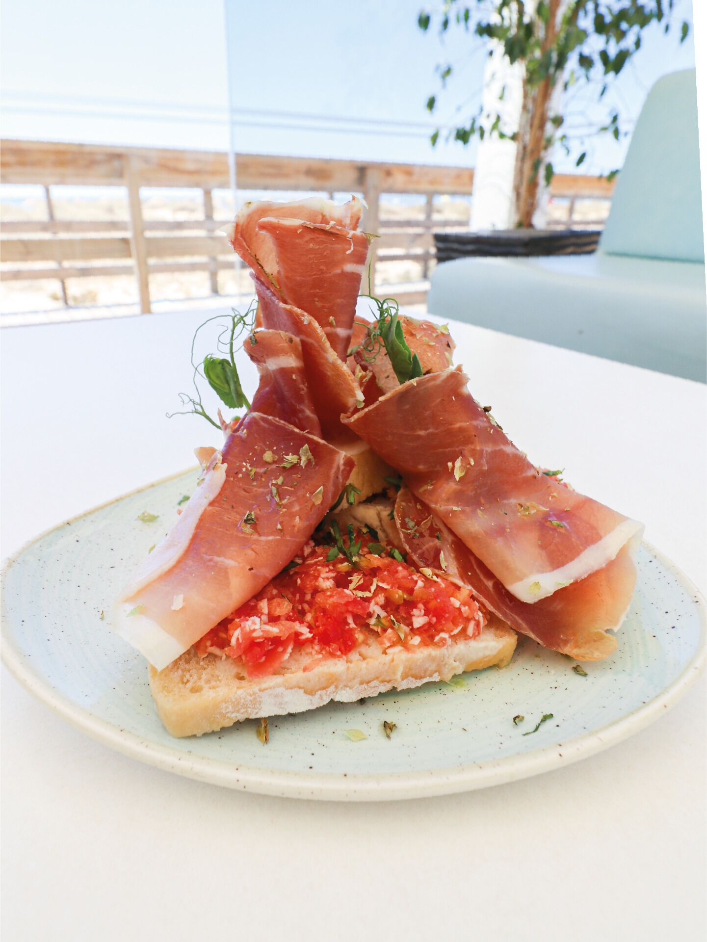 Un plato con jamón serrano y tomate sobre una rebanada de pan.