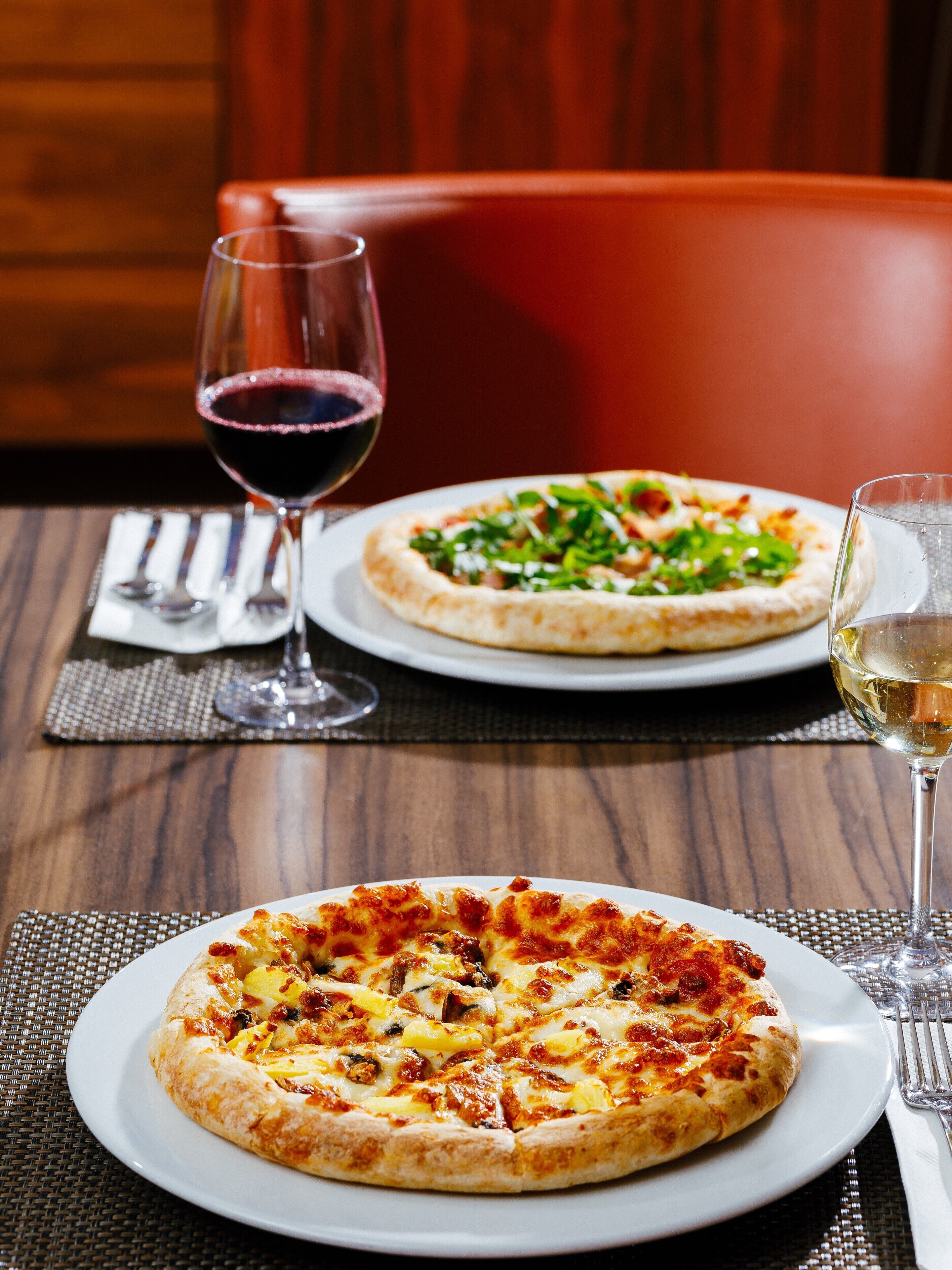 A dining table with two pizzas and two glasses of wine.