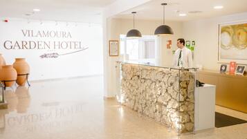 Un mostrador de recepción con fachada de piedra, una lámpara de araña moderna y un cartel que indica Vilamoura Garden Hotel.