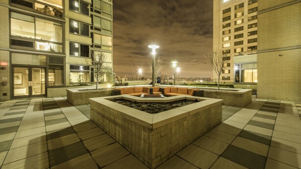Un patio exterior con una zona de estar central, rodeado de edificios con ventanas iluminadas.