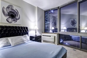 Habitación de hotel con una cama grande, ventana con vista a la ciudad, aire acondicionado de pared y un cuadro decorativo de flores.