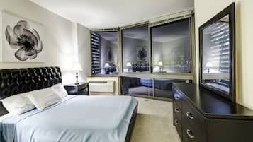 A modern hotel room with a large bed, a dresser, a vanity, and a large window with a city view.