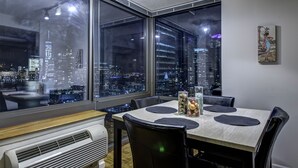 Un área de comedor con vista a la ciudad, una mesa con individuales, un jarrón decorativo y una obra de arte en la pared.