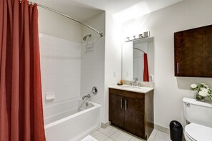 Un bany modern amb una banyera, una dutxa, un lavabo amb mirall i un vàter.