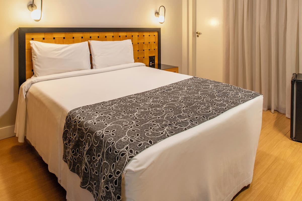 Een net opgemaakt bed met een houten hoofdbord, twee wandlampen en een plafondventilator.