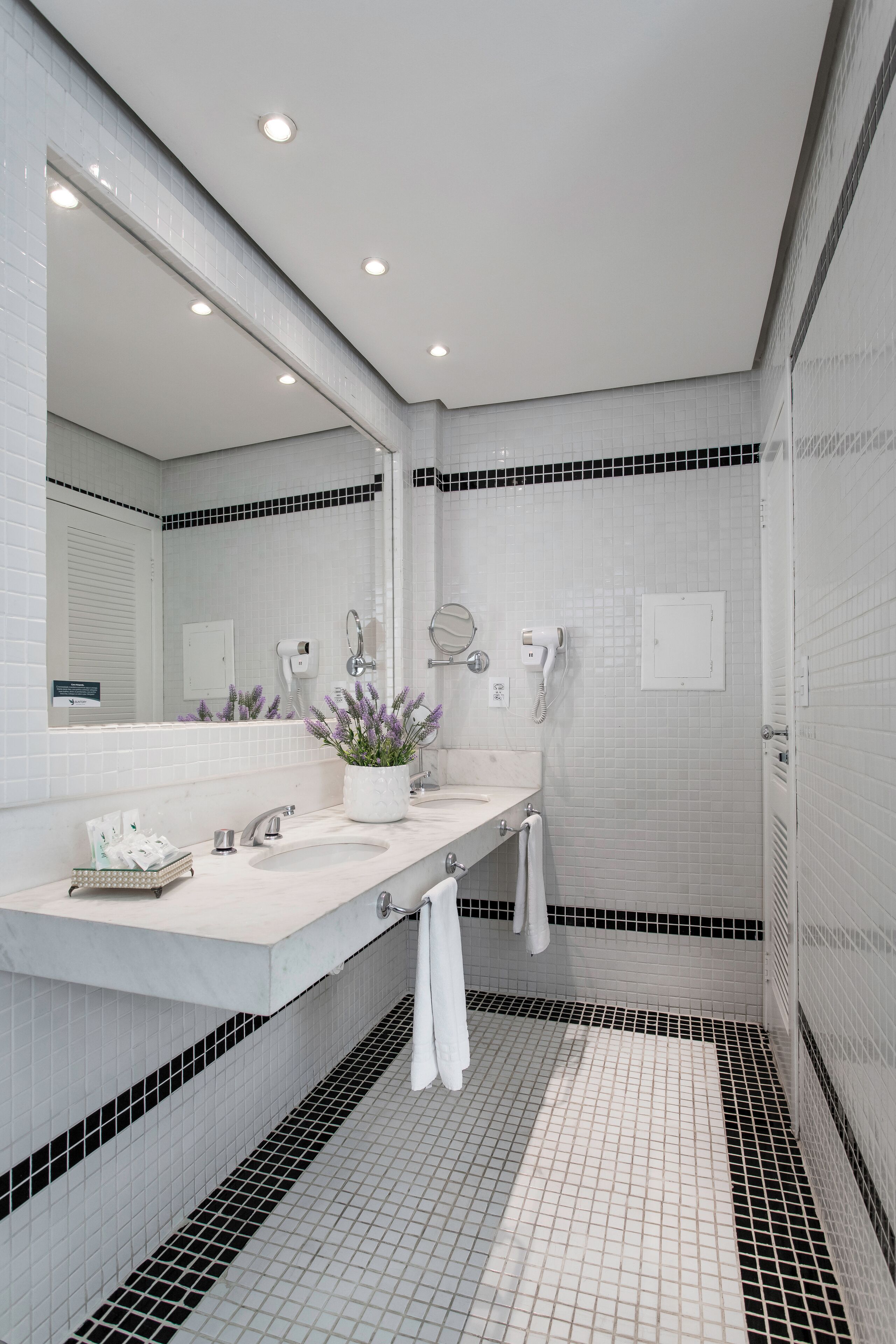 A modern bathroom with two sinks, a large mirror, a hairdryer, and a towel rack.