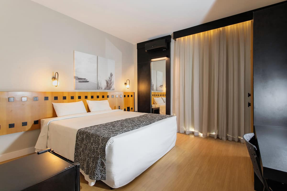 Een moderne hotelkamer met een groot bed, een houten hoofdbord, een nachtkastje en een grote spiegel.