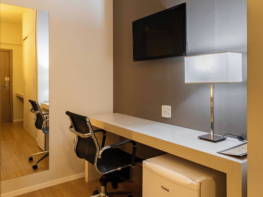 A modern office space with a desk, chairs, a television, and a refrigerator.