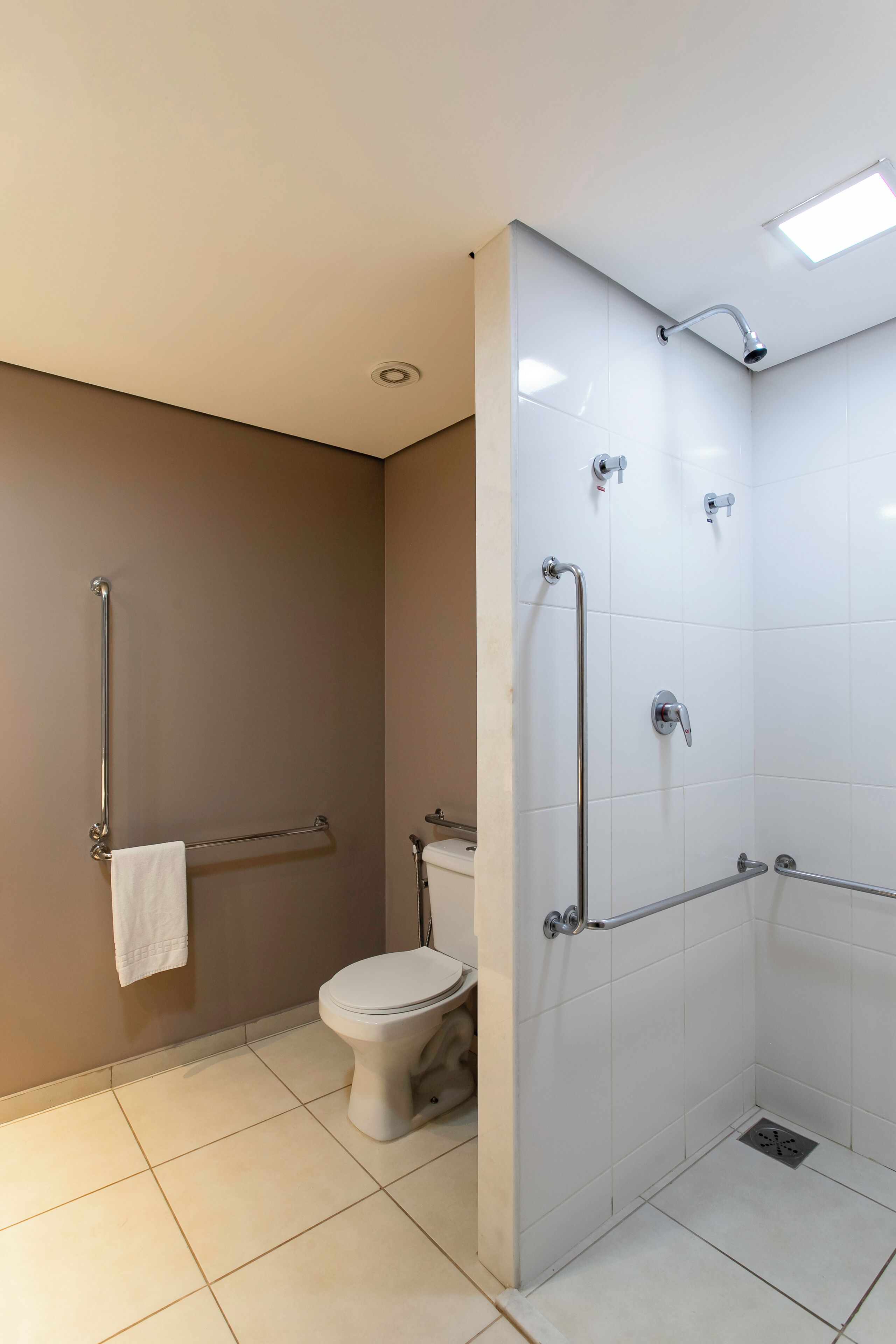 A bathroom with a toilet, a shower with grab bars, and a towel rack.