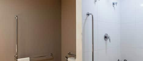 A bathroom with a toilet, a shower with grab bars, and a towel rack.