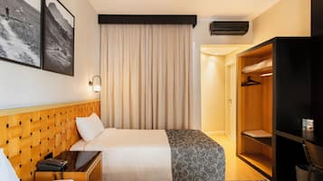 Quarto de hotel com duas camas, cabeceira de madeira, guarda-roupa e ar condicionado fixado na parede.