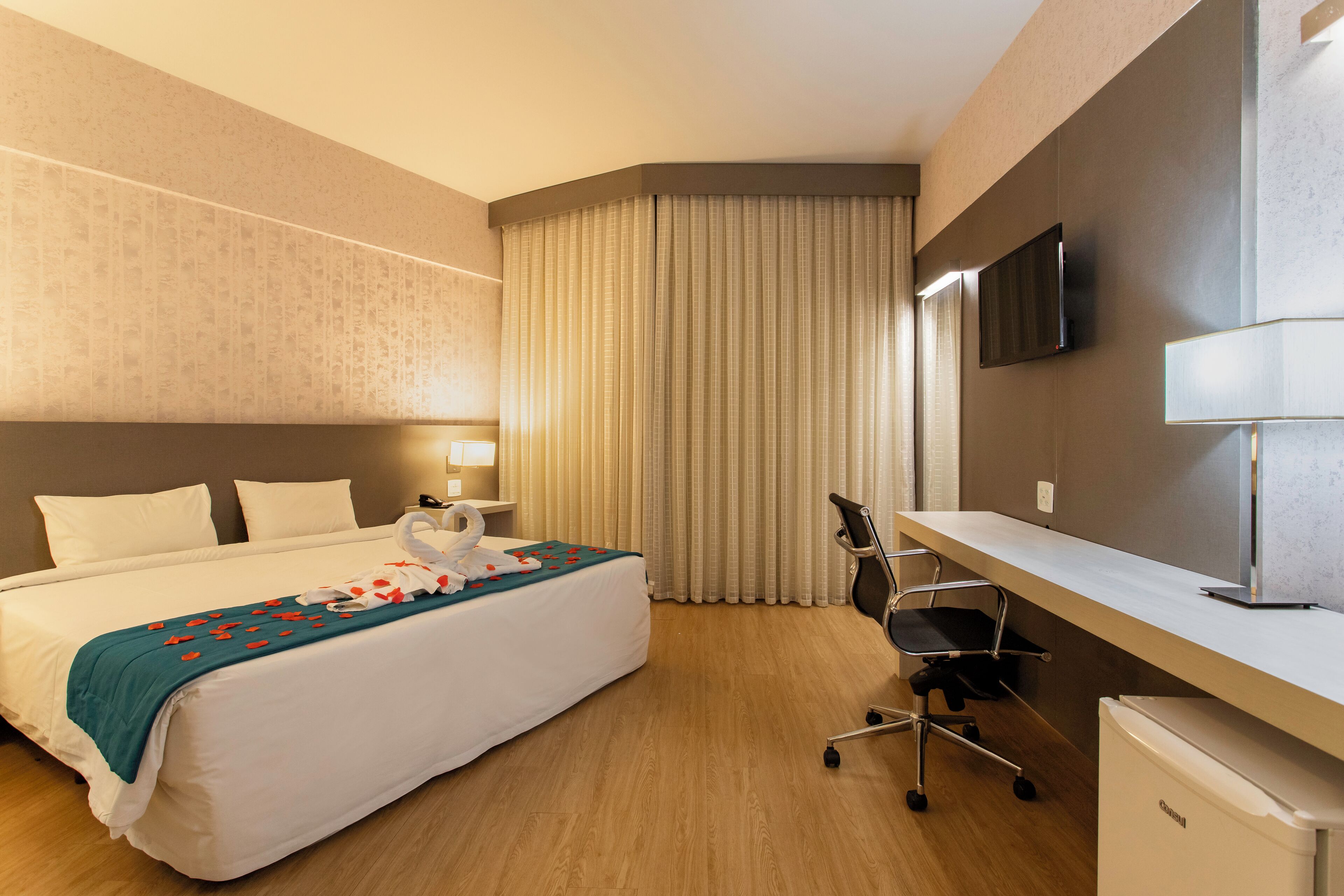 Une chambre d’hôtel équipée d’un lit, d’un bureau, d’une chaise, d’une télévision et d’un petit réfrigérateur.