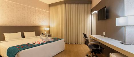 A hotel room with a bed, a desk, a chair, a television, and a small refrigerator.