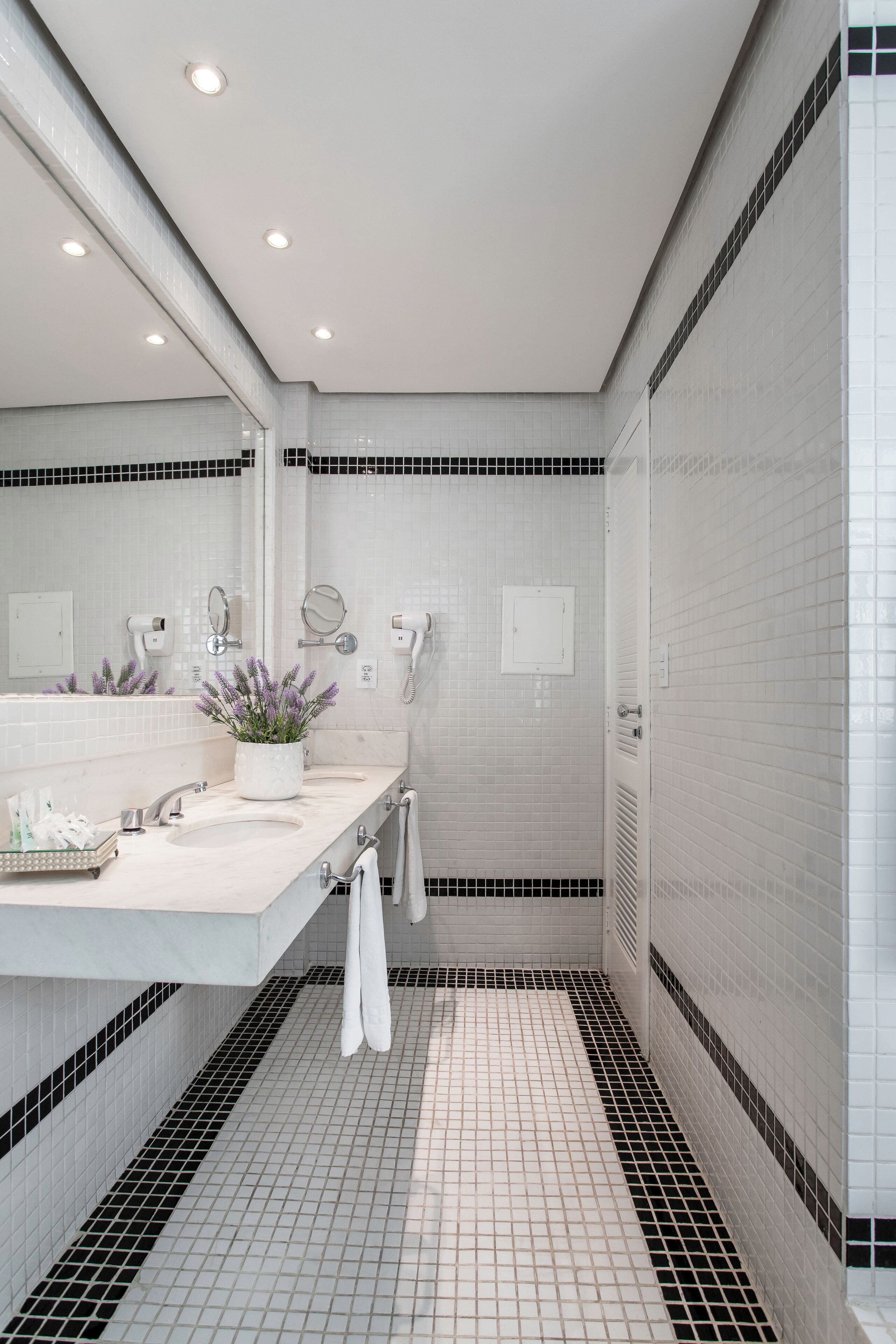 Un baño moderno con azulejos blancos, un espejo grande, un lavamanos y una planta en maceta.