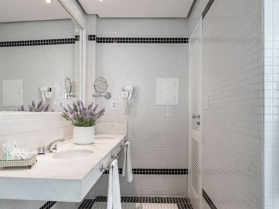 Uma casa de banho moderna com azulejos brancos, um espelho grande, uma pia e uma planta em vaso.