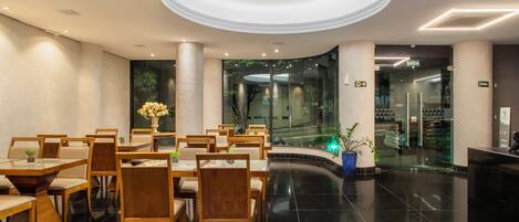 A modern hotel lobby with a circular ceiling design, a reception desk, and a seating area with tables and chairs.