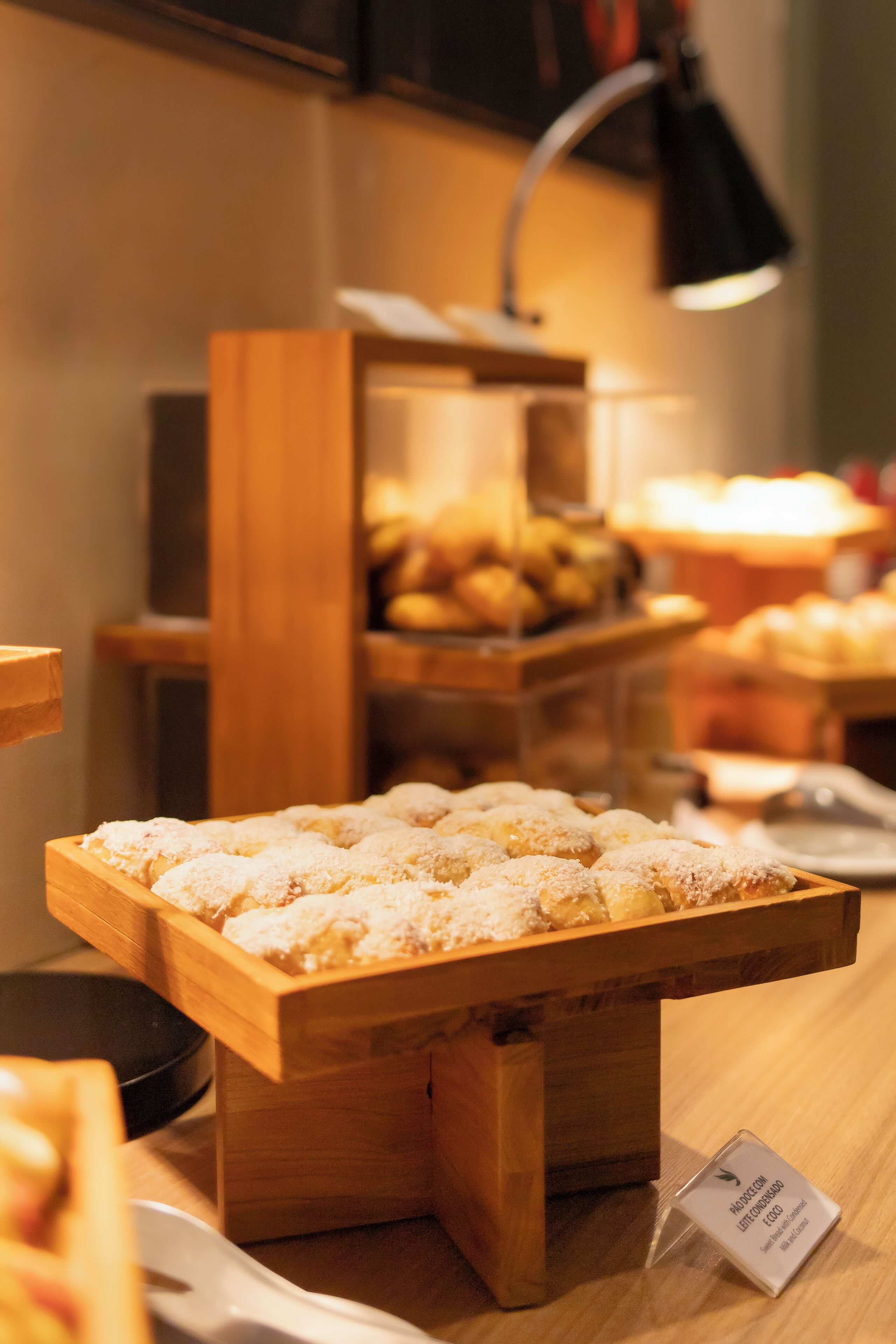 A wooden display stand with pastries, a sign indicating a location, and a lamp in the background.