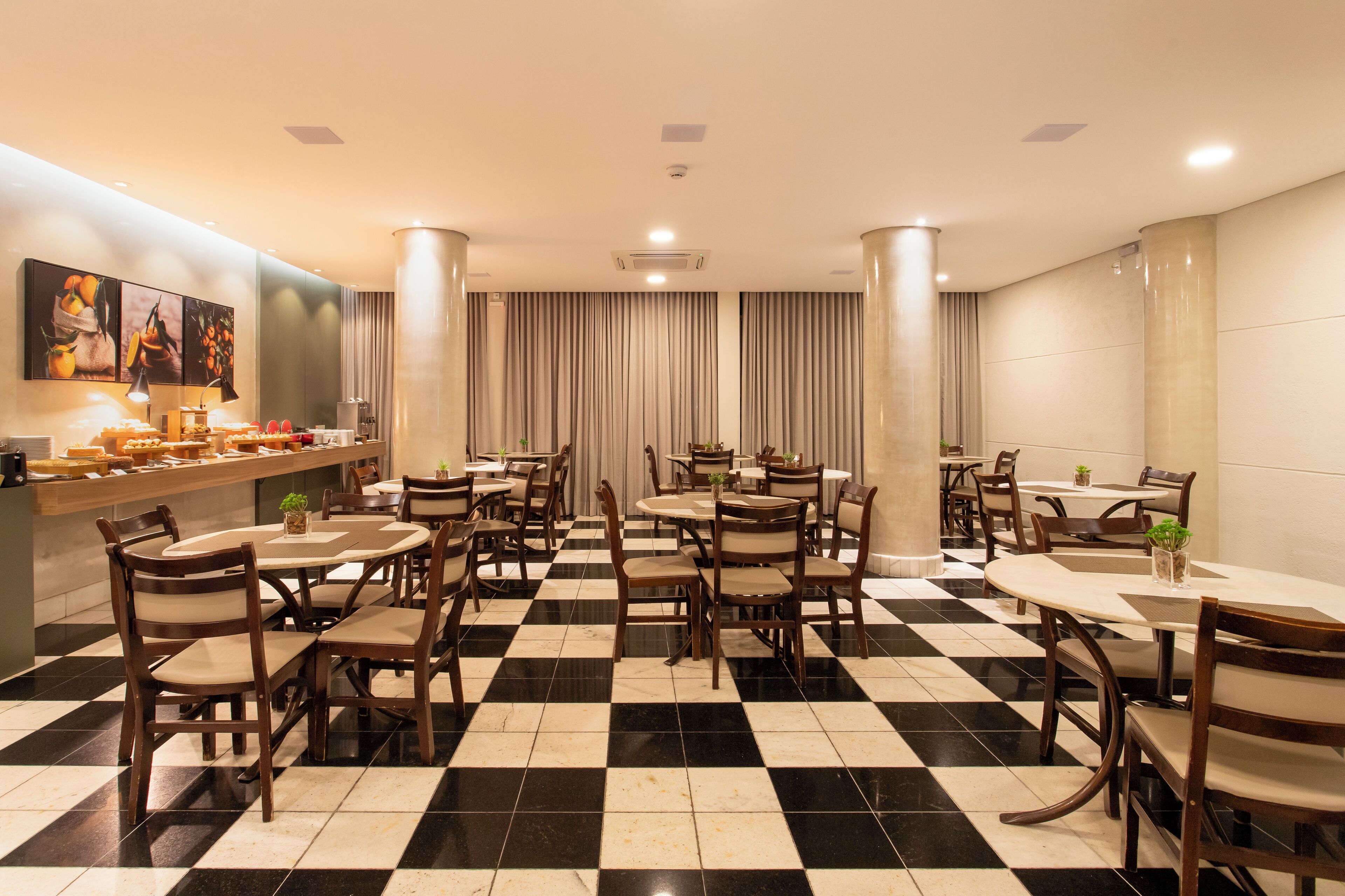 A hotel dining area with checkered flooring, round tables, and wooden chairs.