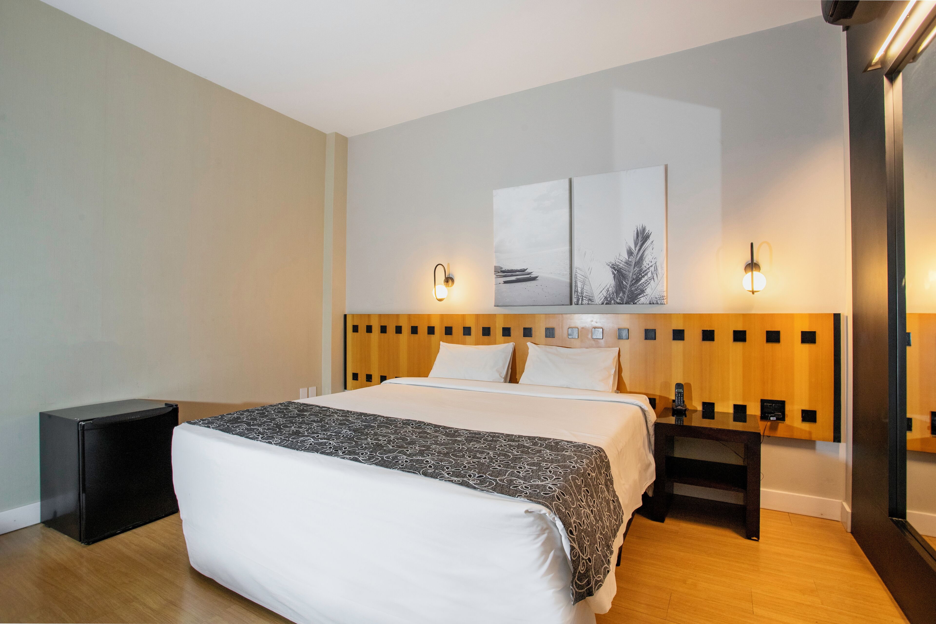A neatly made bed with a patterned bedspread, a bedside table with a lamp, and a wall-mounted artwork above the bed.
