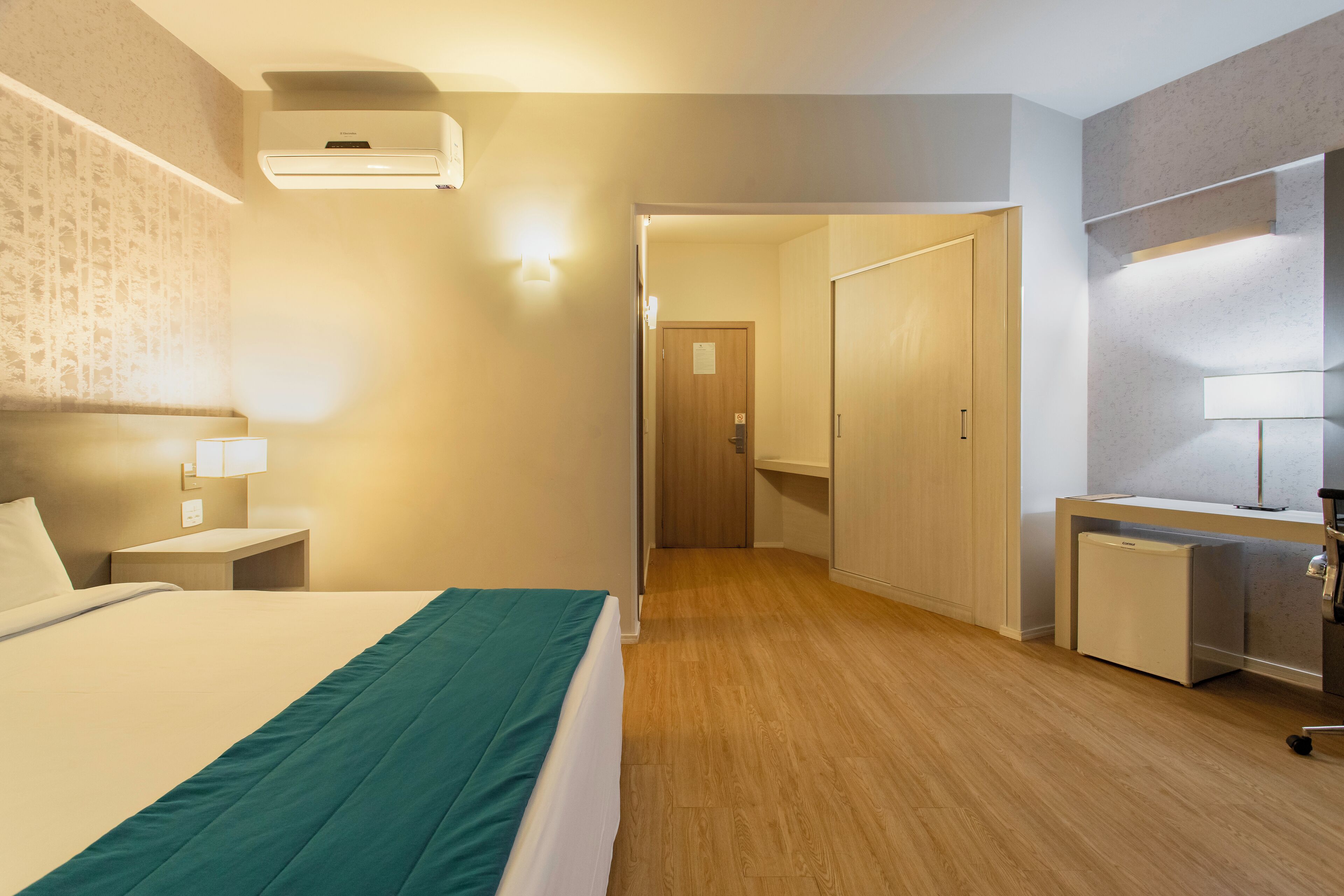 A hotel room with a bed, bedside tables, a desk, and a wardrobe.
