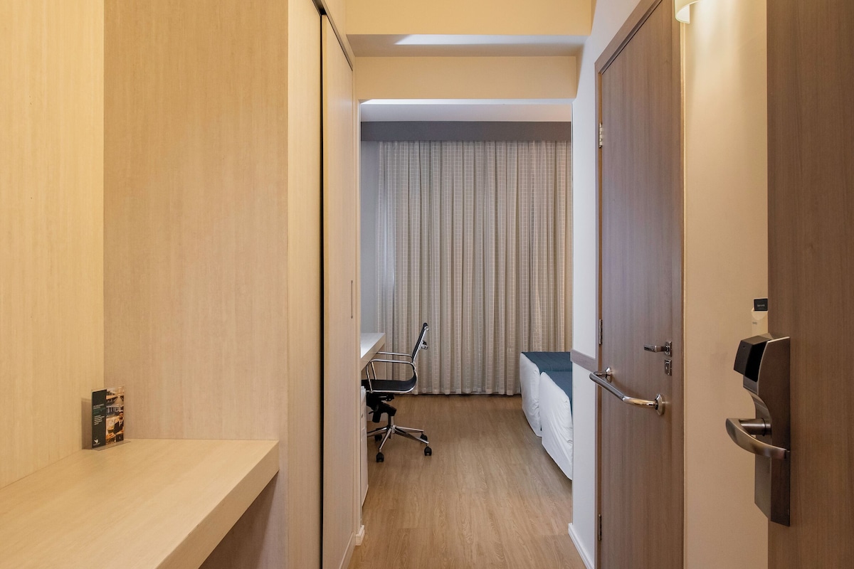 Un pasillo de hotel con suelo de madera, un escritorio con silla, una cama con cortinas y una puerta con cerradura.