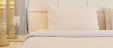 Ein Hotelzimmer mit einem ordentlich bezogenen Bett, einer Nachttischlampe und einer einzelnen roten Rose auf dem Bett.